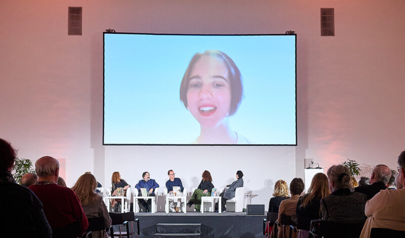 Podiumsdiskussion mit großem Projektorbild im Hintergrund