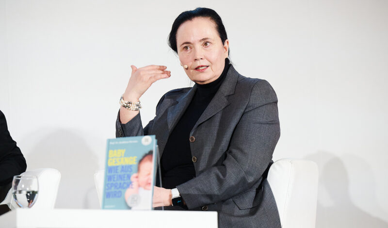 Frau spricht mit Mikrofon, Buch auf Tisch.